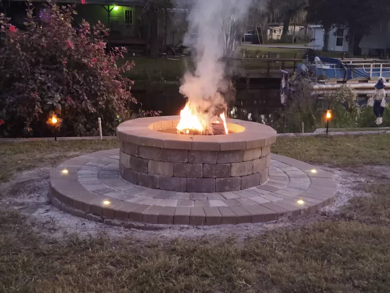 waterfront paver fire pit with fire burning at dusk