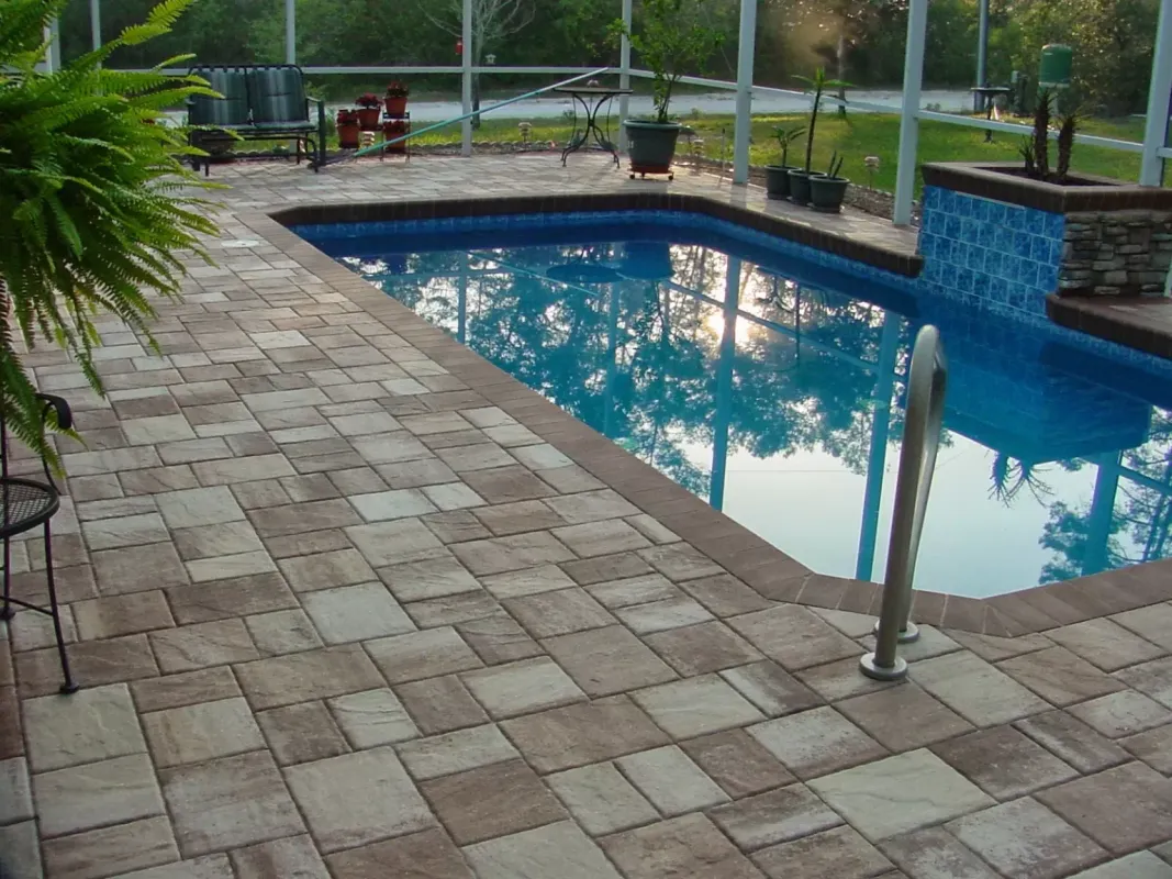 A large swimming pool is surrounded by a brick patio