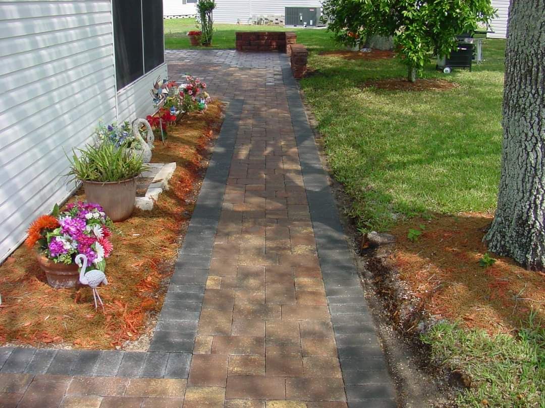 A brick walkway leading to a house with flowers on the side.