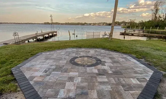A patio with a circular design in the middle of it next to a body of water.